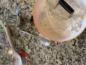 Making Grandma's Homemade Biscuits: Flour, butter, and tools in a bowl on a granite countertop.