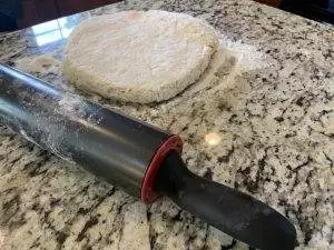 Dough for Grandma's homemade biscuits with rolling pin on granite countertop.